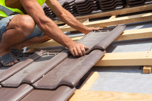 Hands of roofer laying tile on the roof. Installing natural red tile.