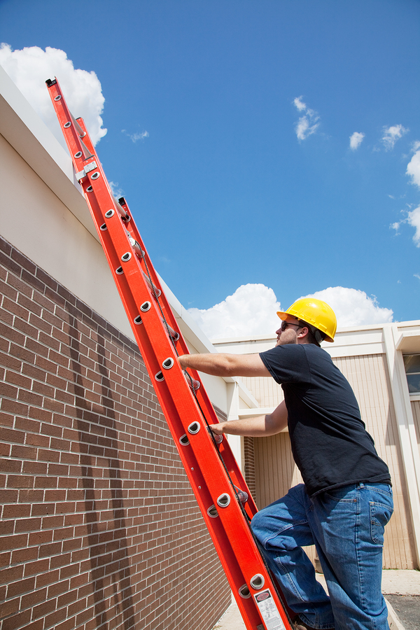 Construction worker climbing up a ladder to the roof of a building.