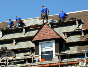 Workers on high roof are replacing old shingles.