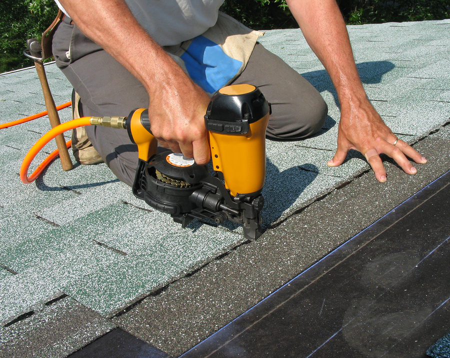 Carpenter uses nail gun to attach asphalt shingles to roof