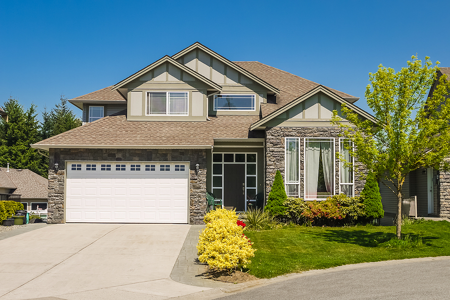 Big family house with concrete driveway to large garage. Residential house entrance with landscaped front yard and a new roof.