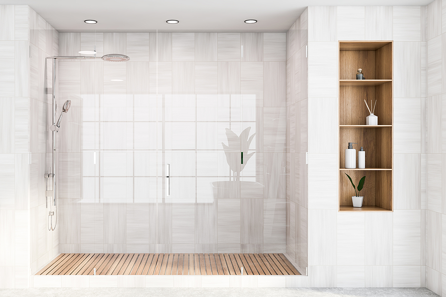 Corner of modern bathroom with white wooden walls, concrete floor, comfortable shower stall with glass doors and shelves with cosmetic products. 