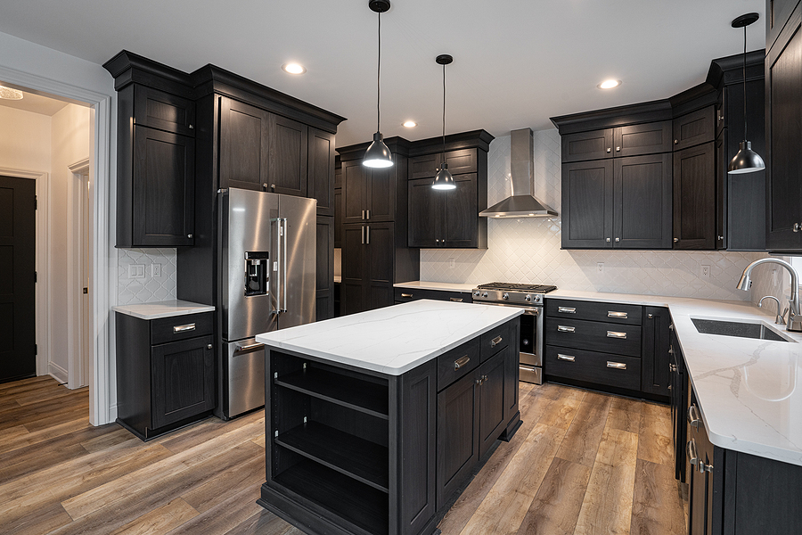 Newly renovated kitchen with black cabinets and white countertops with stainless steel appliances.