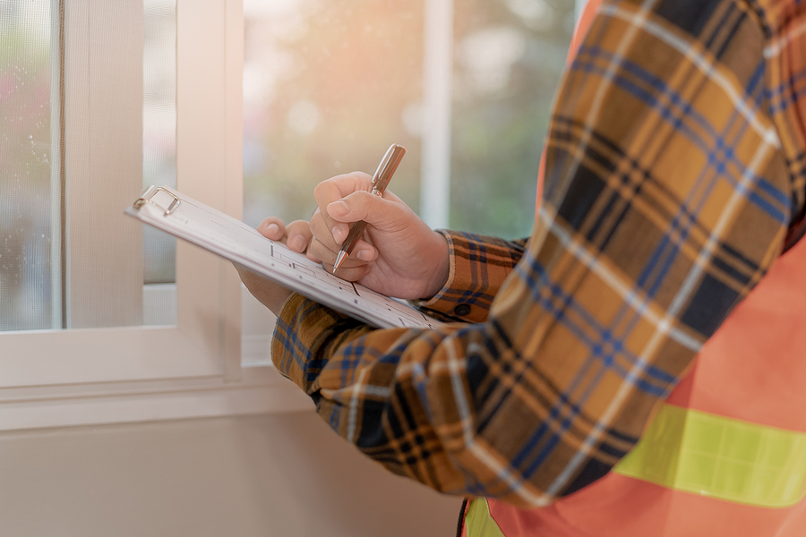 Close up of someone holding a clip board and writing on the paper - standing inside a home wearing a plaid shirt and hi-vis vest