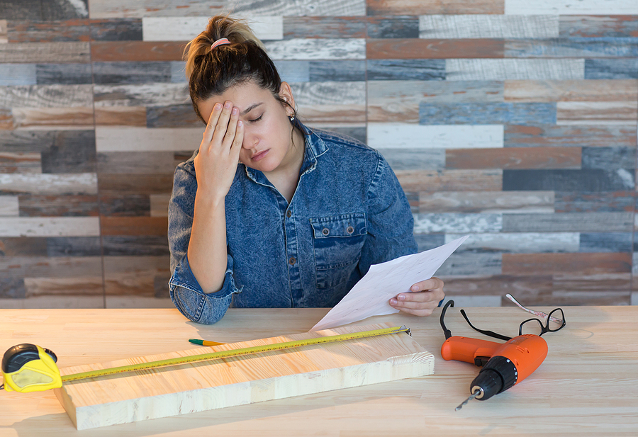 Young woman stressed out trying to do a DIY home improvement project holding a paper with power tools and wood on the table.