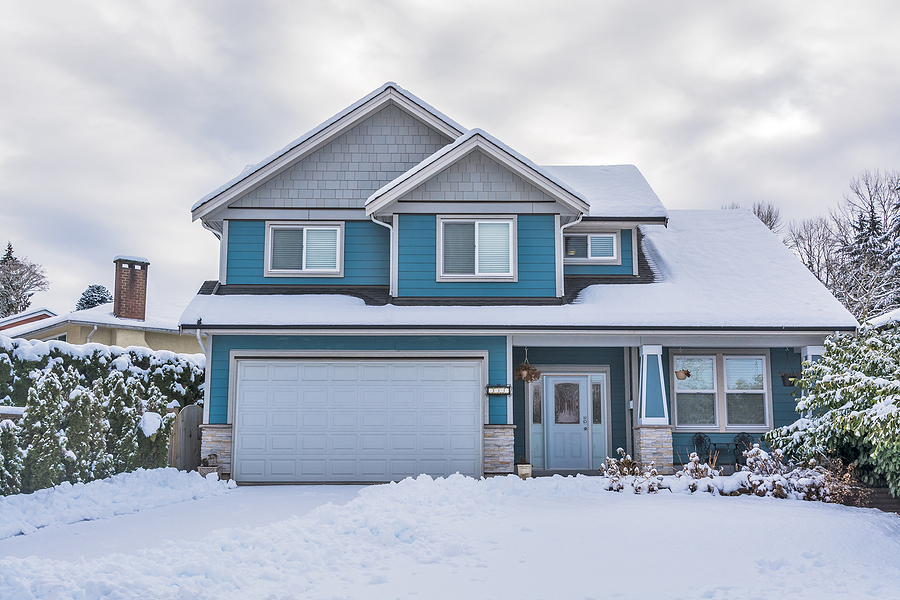 Blue and white two story house covered in snow with snow in lawn and driveway.