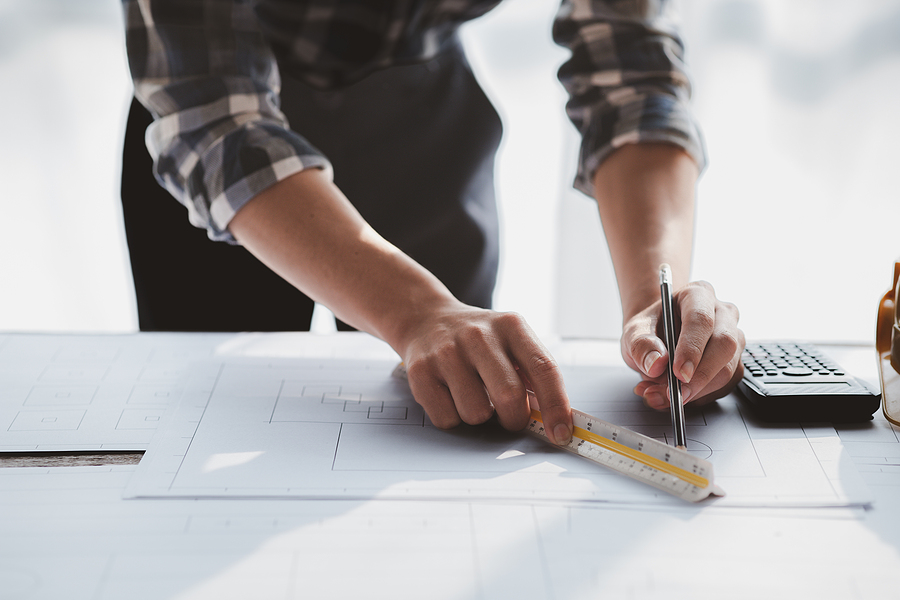 person leaned over a table measuring a blueprint with a ruler and marking with a pen