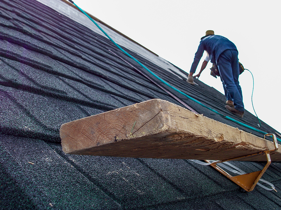 close up of support bracket for shingle installation with roofer working in the background