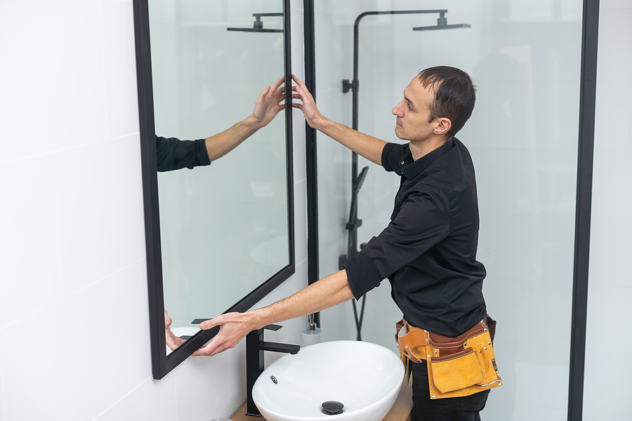 contractor hanging a mirror onto the wall of a newly remodeled bathroom