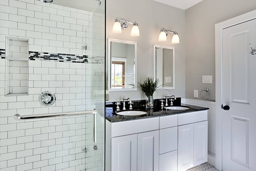 Newly remodeled white bathroom with modern tiled shower and dual sink vanity. 