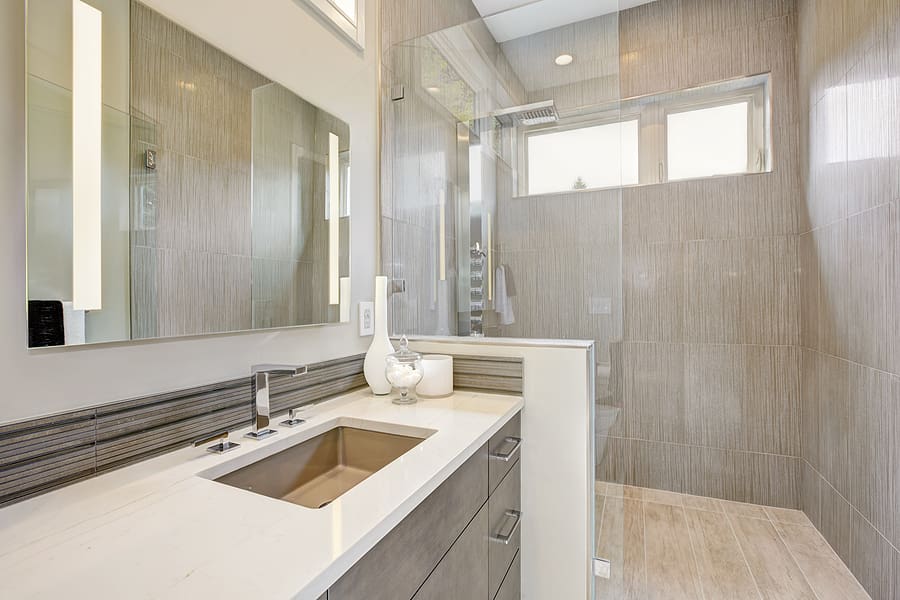 Modern, renovated bathroom with a grey vanity and white countertop and walk-in shower. 